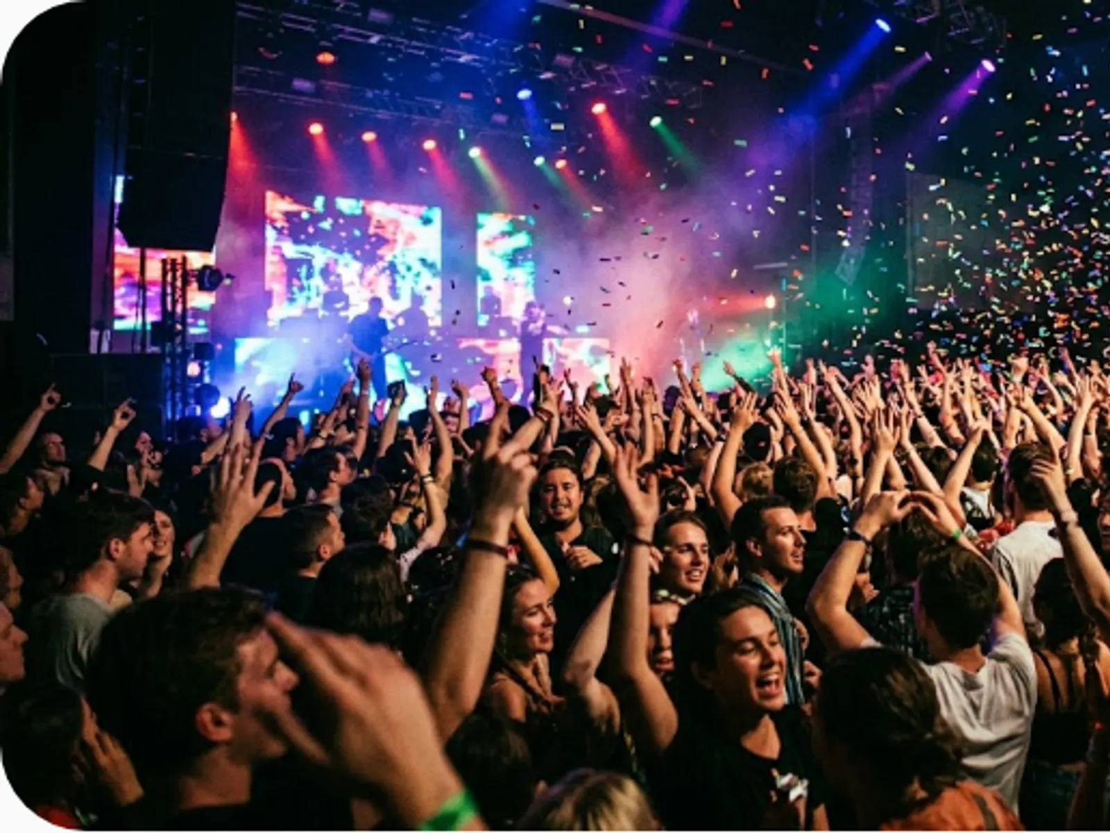 concert audience with raised hands and confetti in coloured light